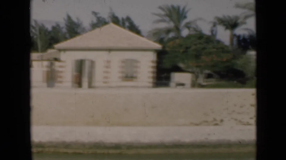 1946 Suez Canal frame showing a pale house with a low roof, palms, trees, and a broad sandy foreground.