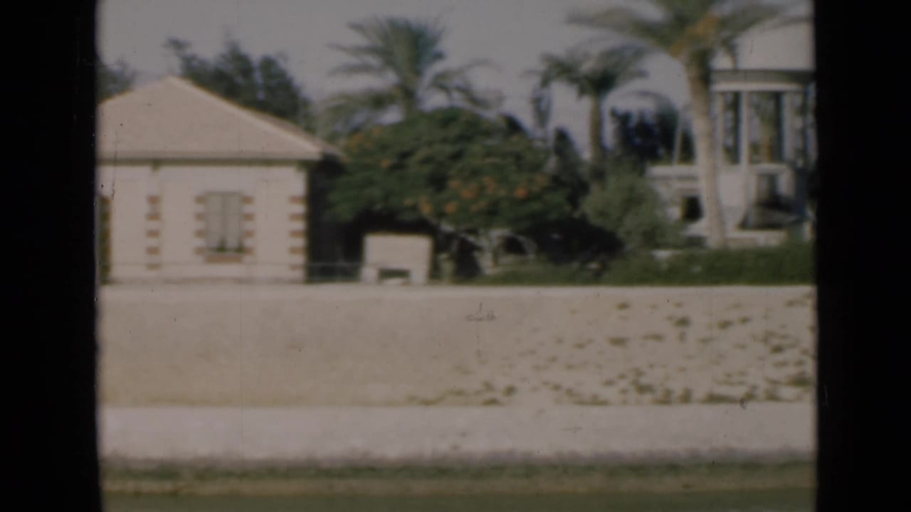 1946 Suez Canal home-movie frame showing a white gabled building, palms, garden wall, and sunlit landscaping.