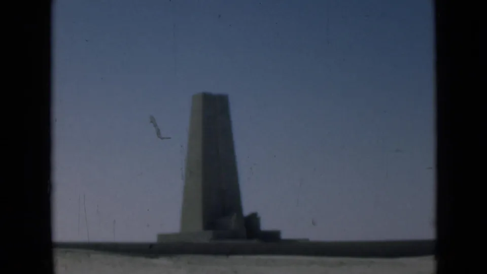 1946 Suez Canal region frame of a distant obelisk-like monument under a clear blue sky, with visible film dust and gate edges.