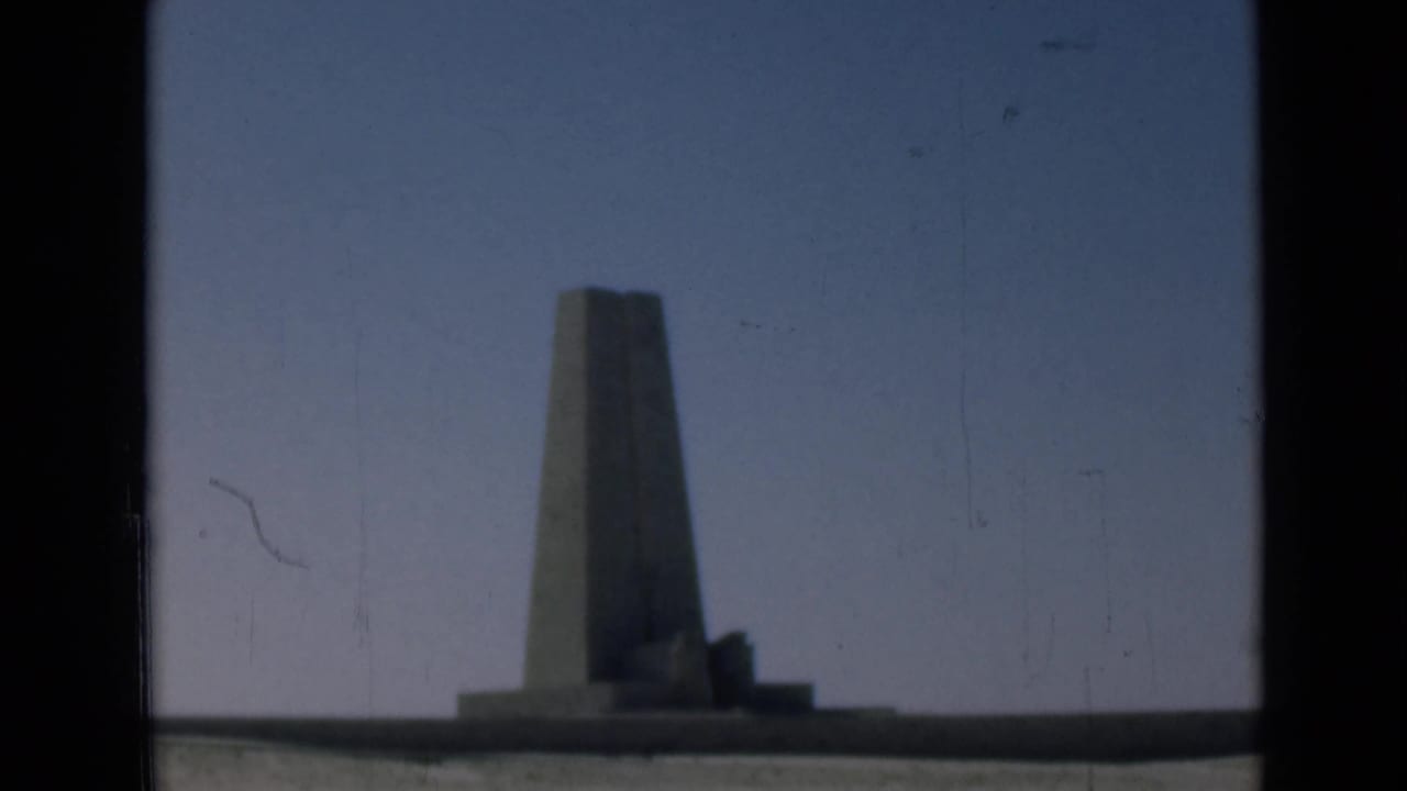 1946 Suez Canal region home-movie frame holding on a distant obelisk-like monument, with muted color and visible film scratches.