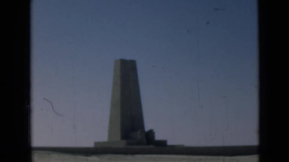 1946 Suez Canal region home-movie frame holding on a distant obelisk-like monument, with muted color and visible film scratches.