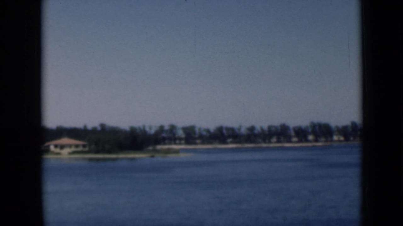 Final 1946 Suez Canal frame with broad blue water, distant trees, low shoreline structures, and visible 8mm film borders.