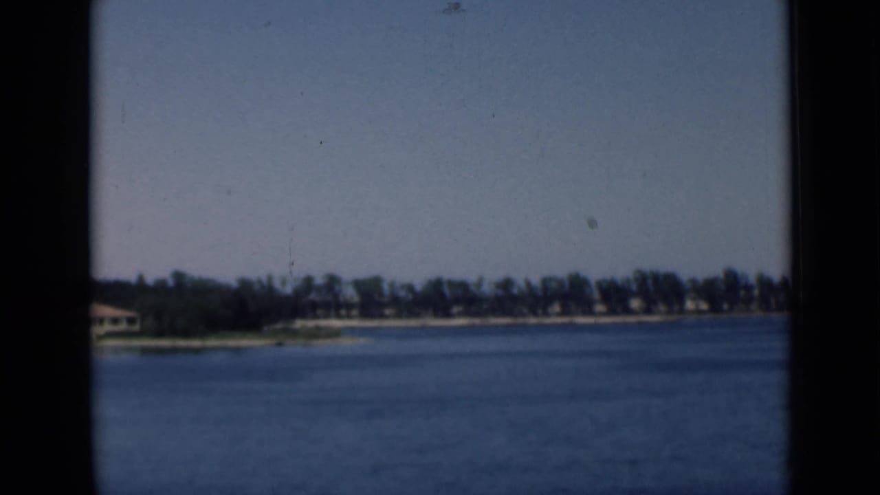 1946 Suez Canal home-movie frame showing blue water, distant trees, low shoreline buildings, and dark 8mm frame borders.