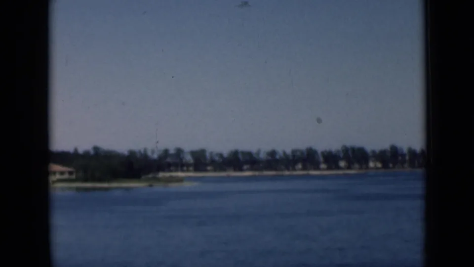 1946 Suez Canal home-movie frame showing blue water, distant trees, low shoreline buildings, and dark 8mm frame borders.