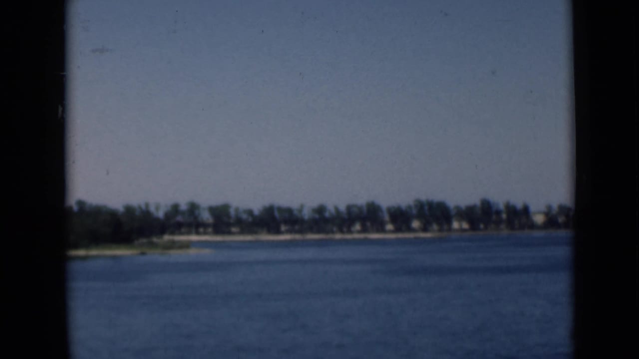 Distant canal shoreline across blue water, framed by dark film borders.