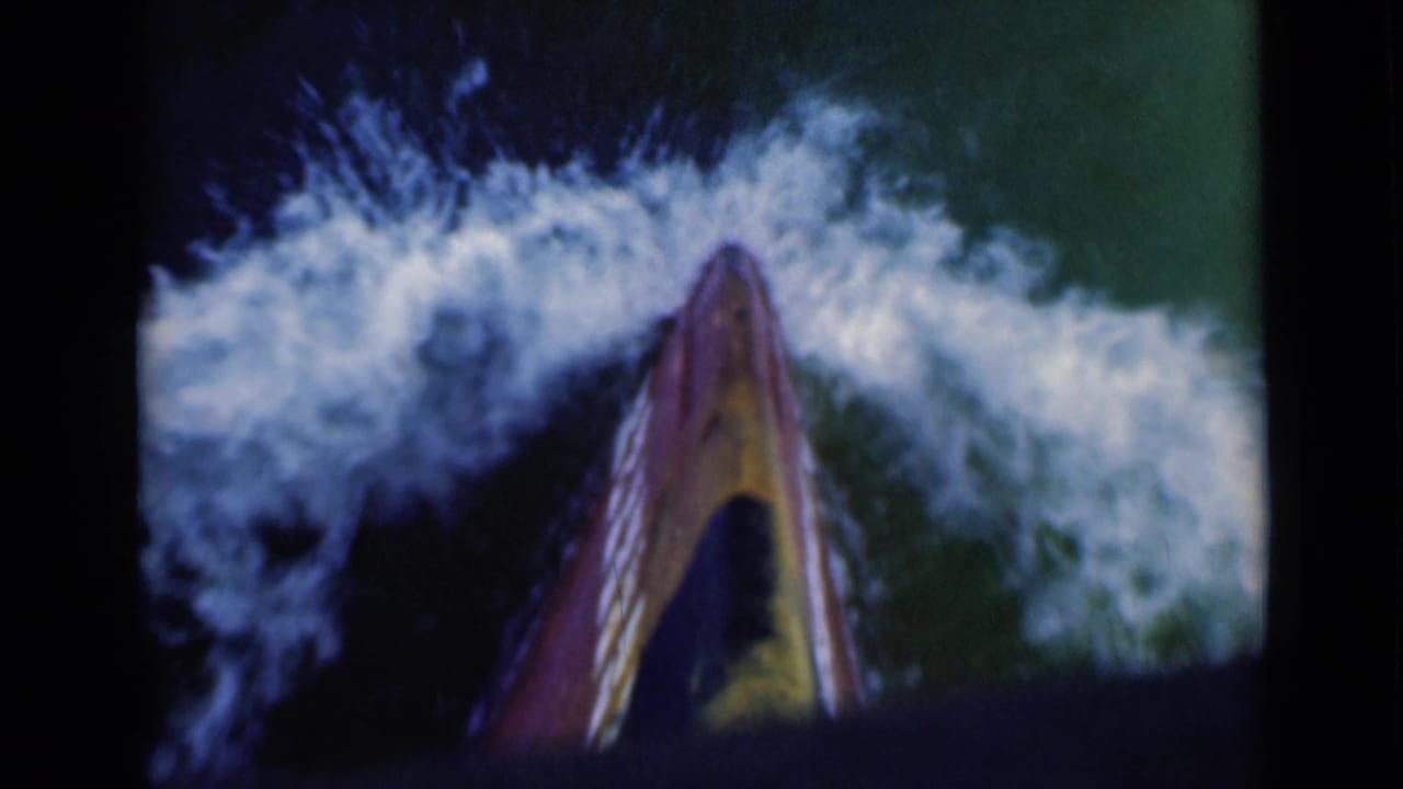 A close traveler’s view over the boat bow shows foaming wake and green-blue water in vintage 8mm maritime footage.