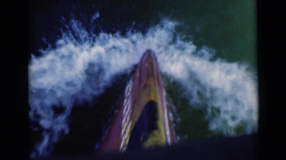 A close traveler’s view over the boat bow shows foaming wake and green-blue water in vintage 8mm maritime footage.