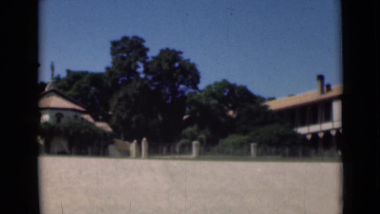 1946 Suez Canal home-movie frame showing a sunlit coastal building behind a pale boundary wall and trees.