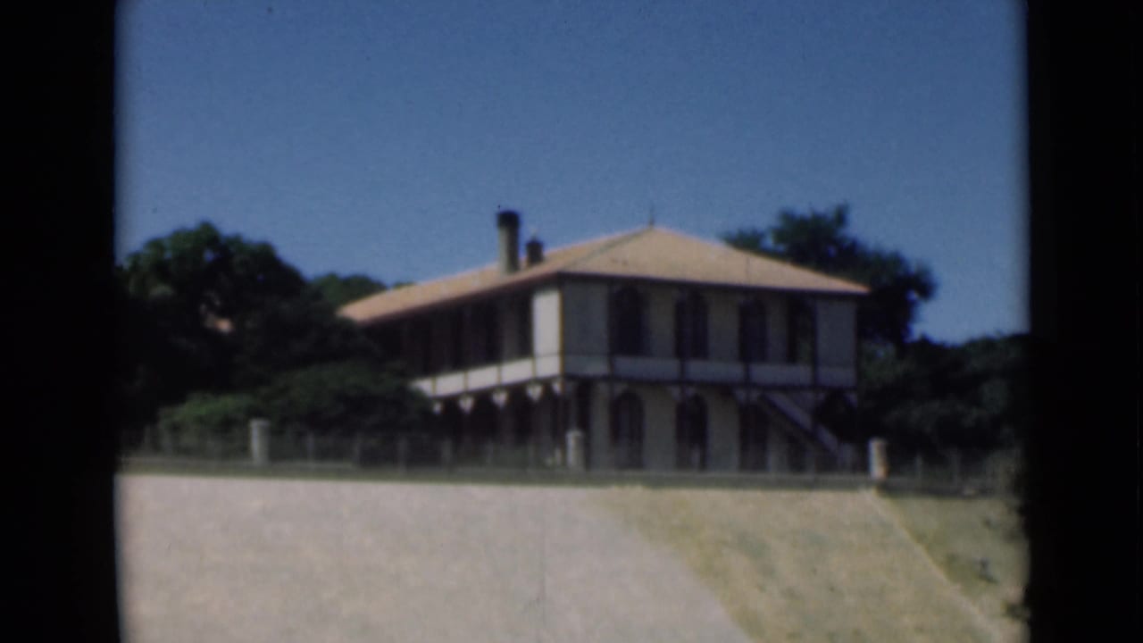 1946 Suez Canal home-movie frame showing a two-story veranda building beside trees and open foreground ground.