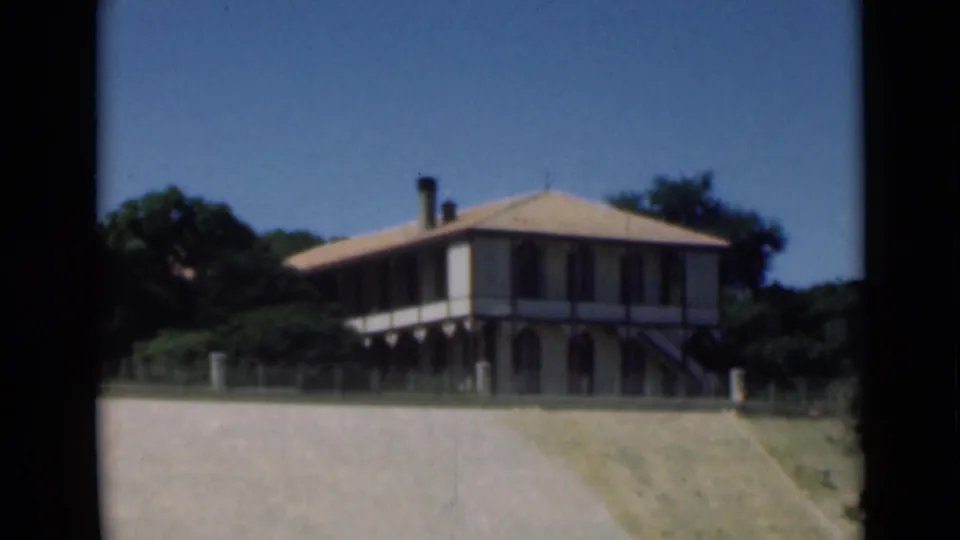 1946 Suez Canal home-movie frame showing a two-story veranda building beside trees and open foreground ground.