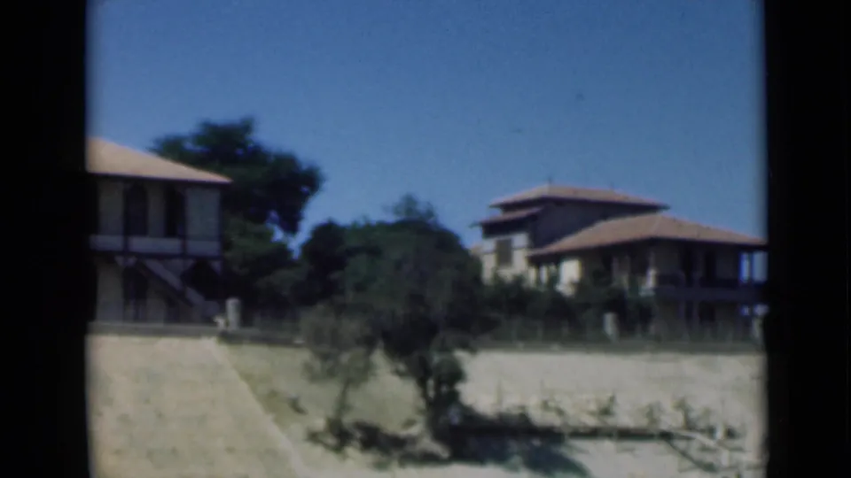 1946 Suez Canal area home-movie frame showing the camera panning past a house edge toward another veranda-fronted residence and trees.