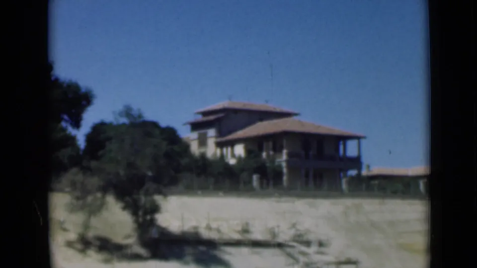1946 Suez Canal area frame showing a two-story house with a broad tiled roof, shaded veranda, trees, open ground, and clear sky.