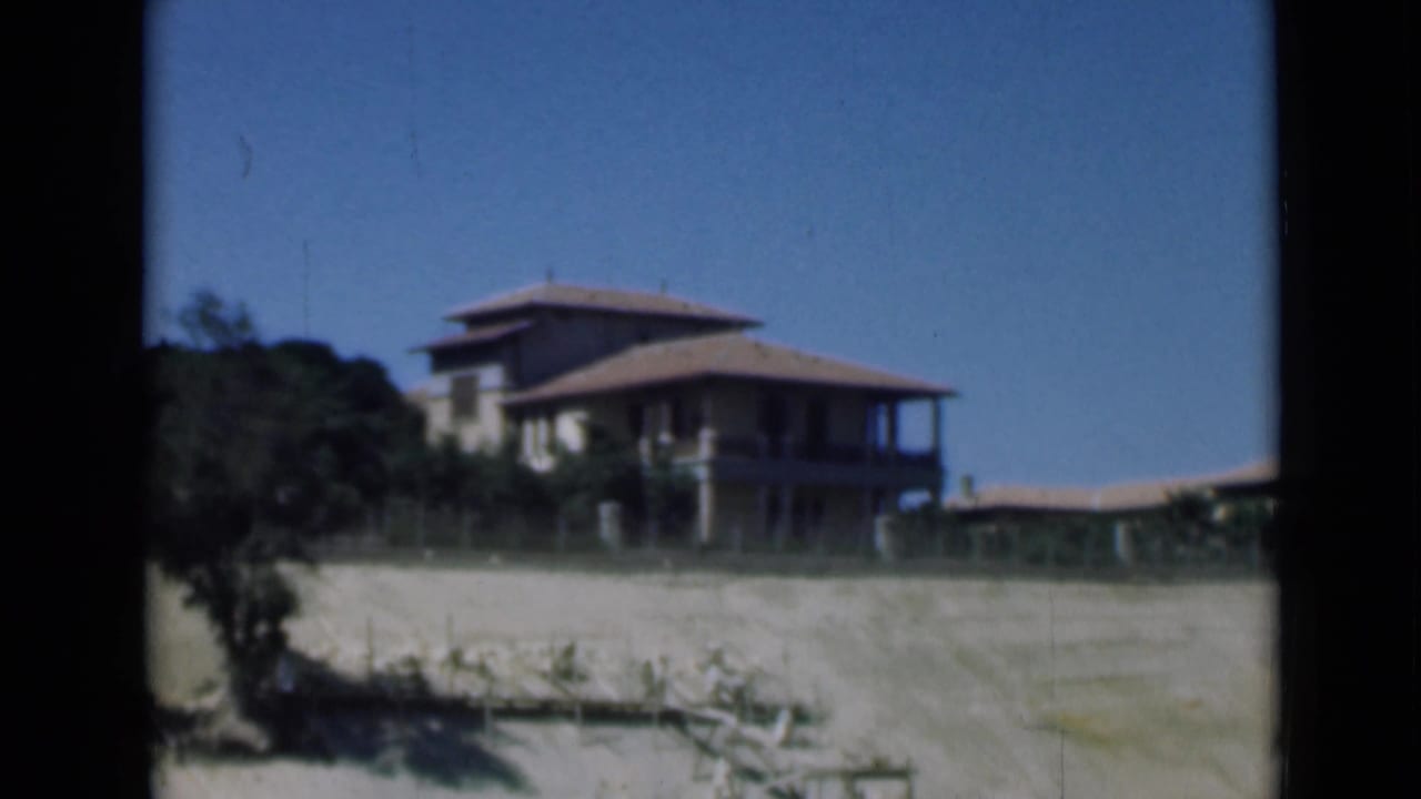 1946 8mm frame of a large shorefront house near the Suez Canal area, with sandy ground, low fencing, and clear sky.