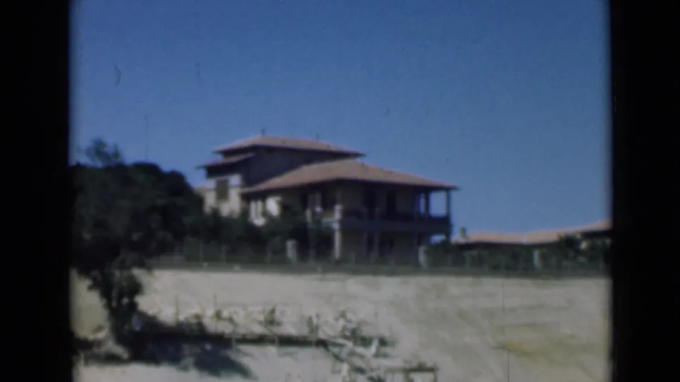 1946 8mm frame of a large shorefront house near the Suez Canal area, with sandy ground, low fencing, and clear sky.