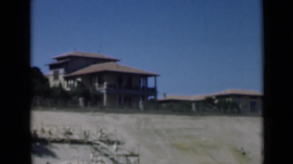 Shorefront buildings near the Suez Canal area appear across pale sand, framed by dark 8mm gate borders and blue sky.