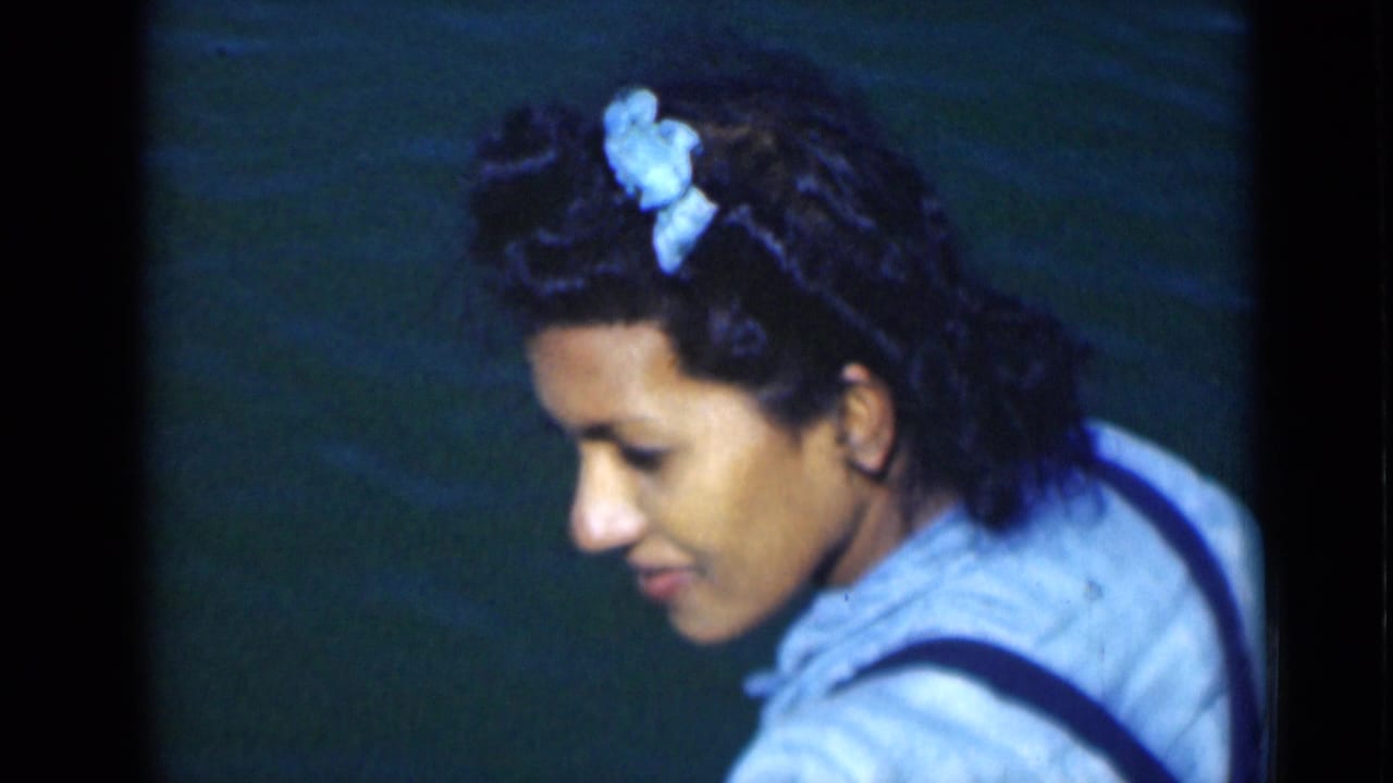 A close home-movie frame shows the woman looking down, her blue bow and light clothing visible beside the water.