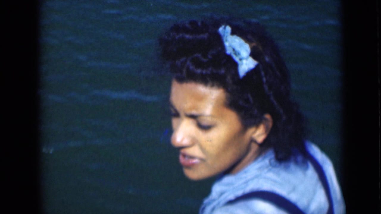 Adult woman with a pale hair bow turns slightly toward the camera, with Suez Canal water behind her in vintage 8mm footage.