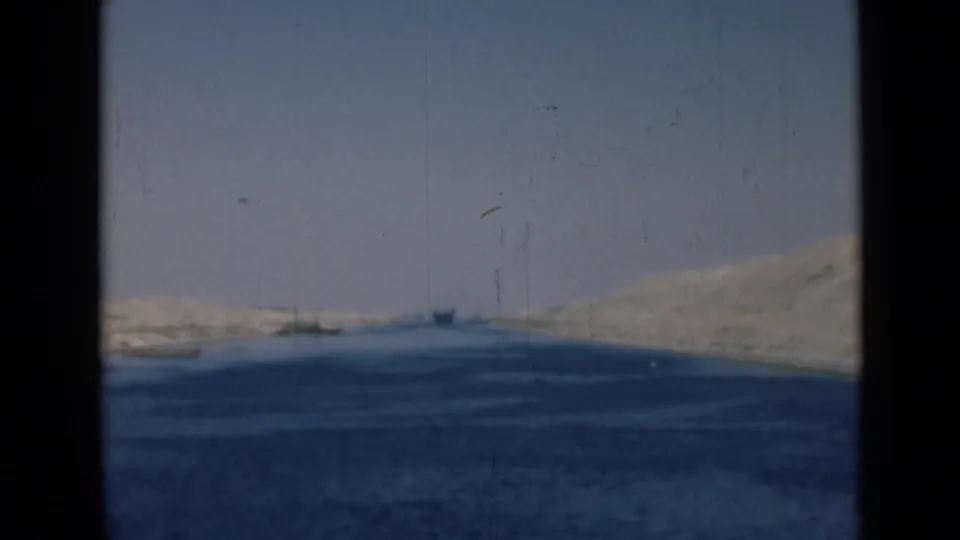 1946 8mm view of the Suez Canal with blue water, sandy banks, distant shapes, and heavy dark frame edges.