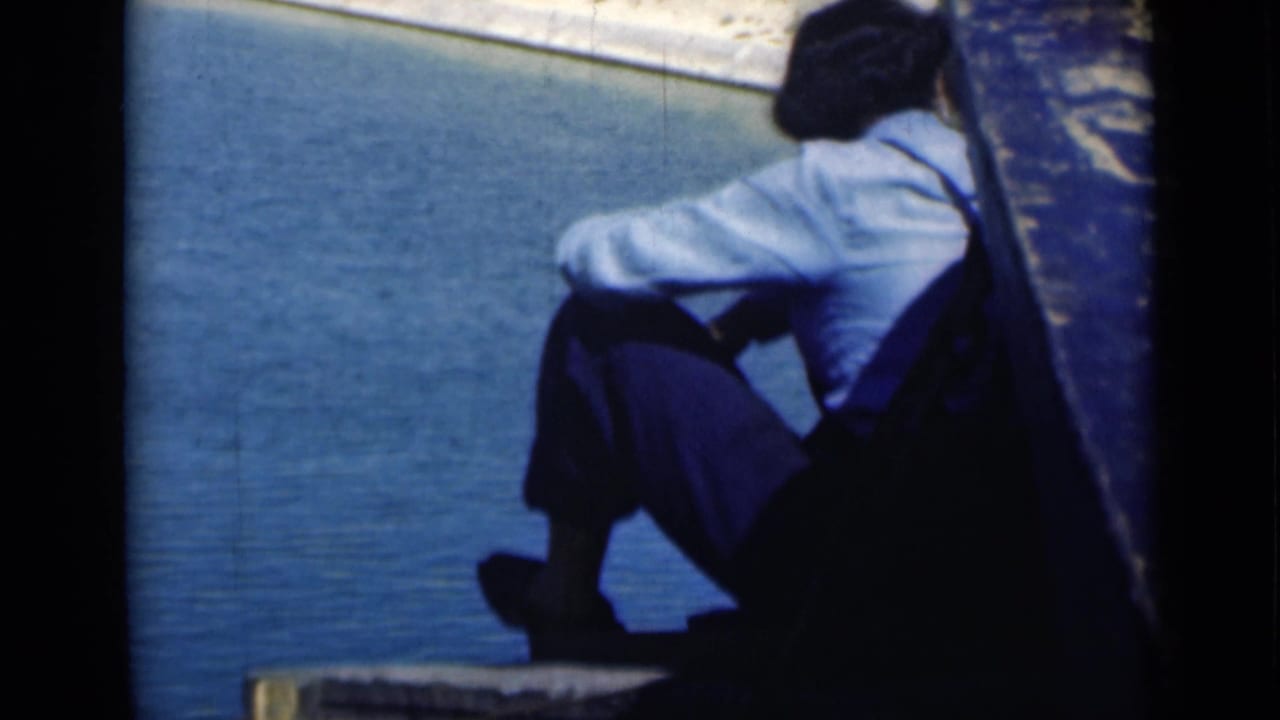 A seated figure rests near the edge of a boat on the Suez Canal, with blue water filling most of the frame.