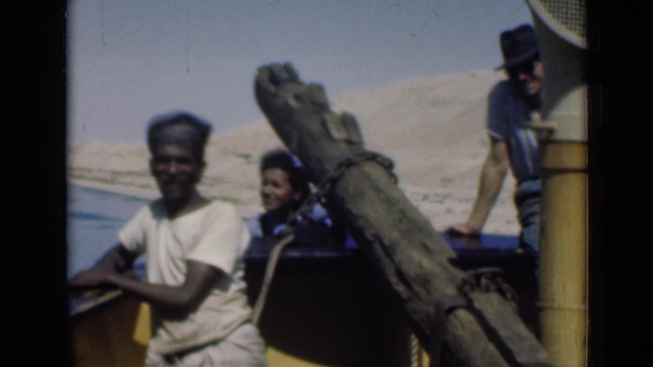 1946 Suez Canal home-movie frame showing three people on a boat, with a man at the side rail and desert bank behind.