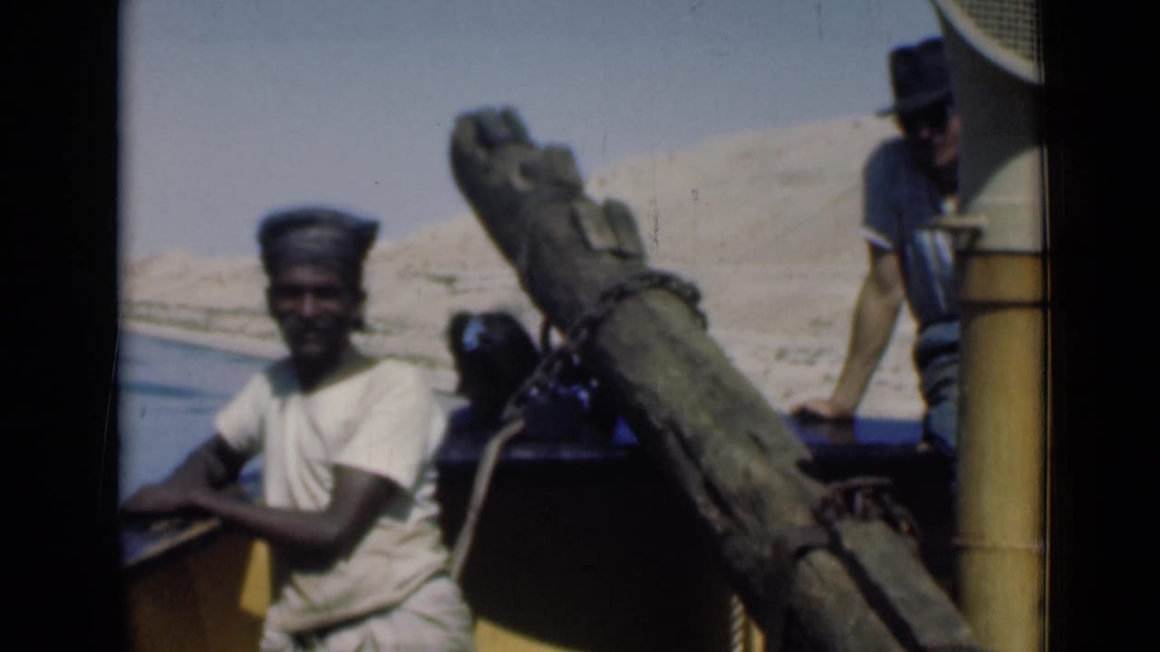 Close 1946 Suez Canal frame with a man near the rail, another person partly obscured, and a man in a hat standing at the stern.