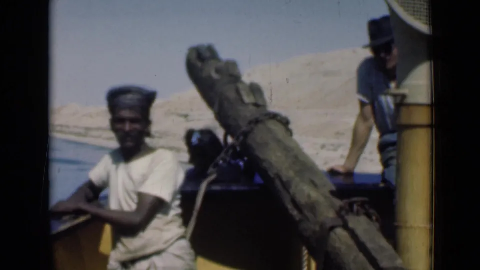 Close 1946 Suez Canal frame with a man near the rail, another person partly obscured, and a man in a hat standing at the stern.