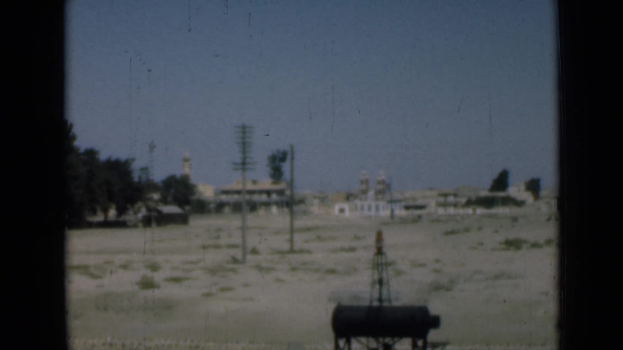 1946 Egypt roadside view near the Suez Canal with pale arid ground, utility poles, distant structures, trees, and a foreground tank.