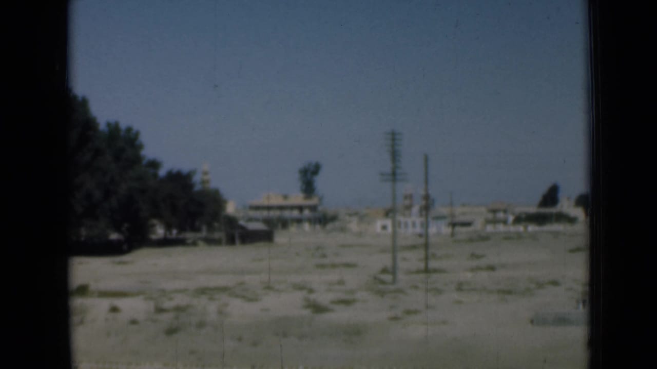1946 Egypt home-movie frame showing sparse land near the Suez Canal with trees, poles, distant buildings, and a small derrick-like form.