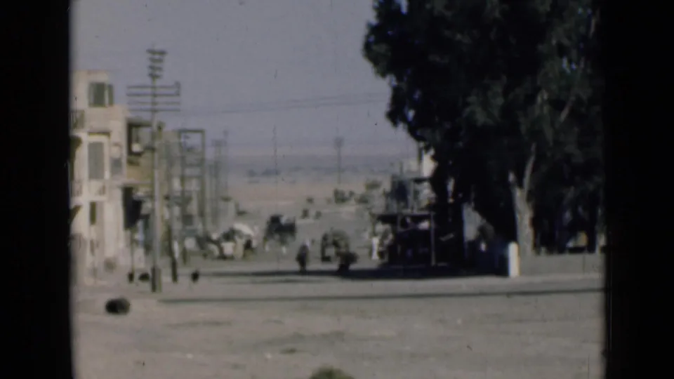 1946 8mm view near the Suez Canal showing a quiet street with buildings, utility poles, trees, pedestrians, and distant vehicles.