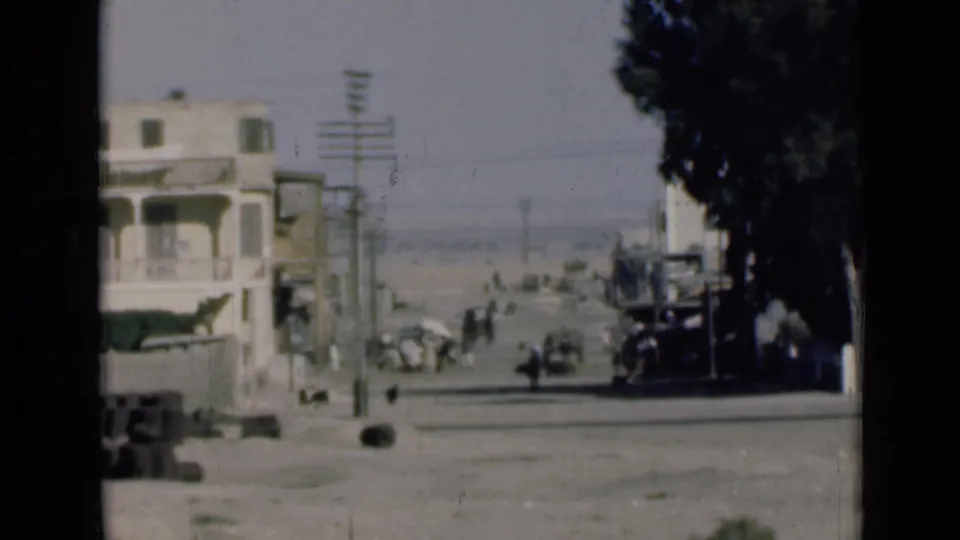 1946 Egypt street view near the Suez Canal with a pale building, roadside trees, utility poles, pedestrians, and early vehicles.