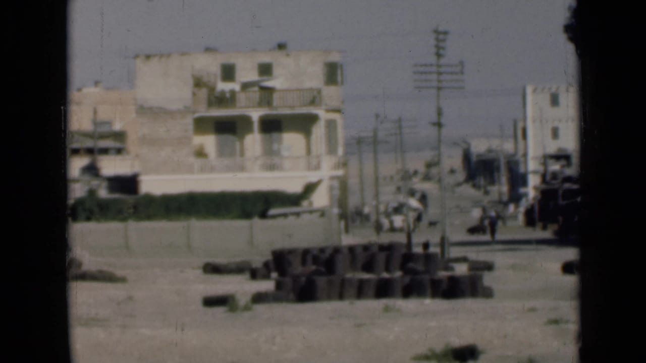 1946 Suez Canal, Egypt view of pale two-story buildings, poles, wires, dusty road, and debris near the shoreline.