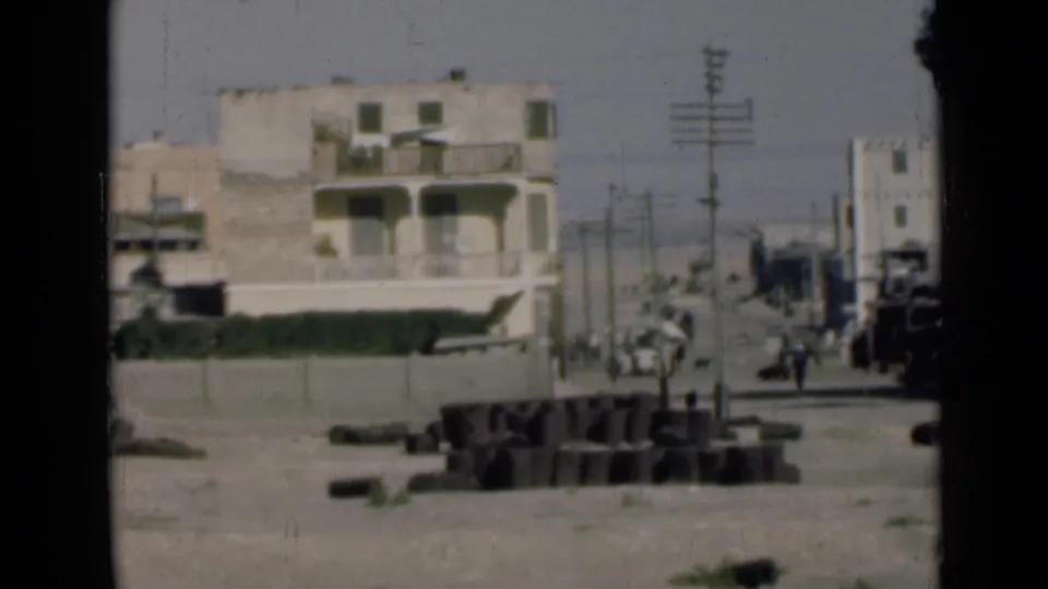 1946 Suez Canal, Egypt view of pale two-story buildings, poles, wires, dusty road, and debris near the shoreline.