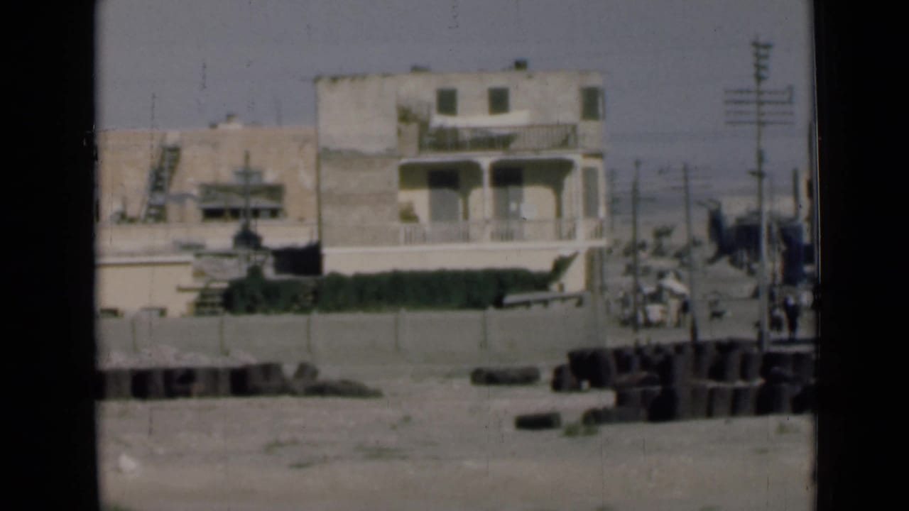 1946 Suez Canal, Egypt street-side view with a balcony building, utility poles, distant pedestrians, and foreground debris.