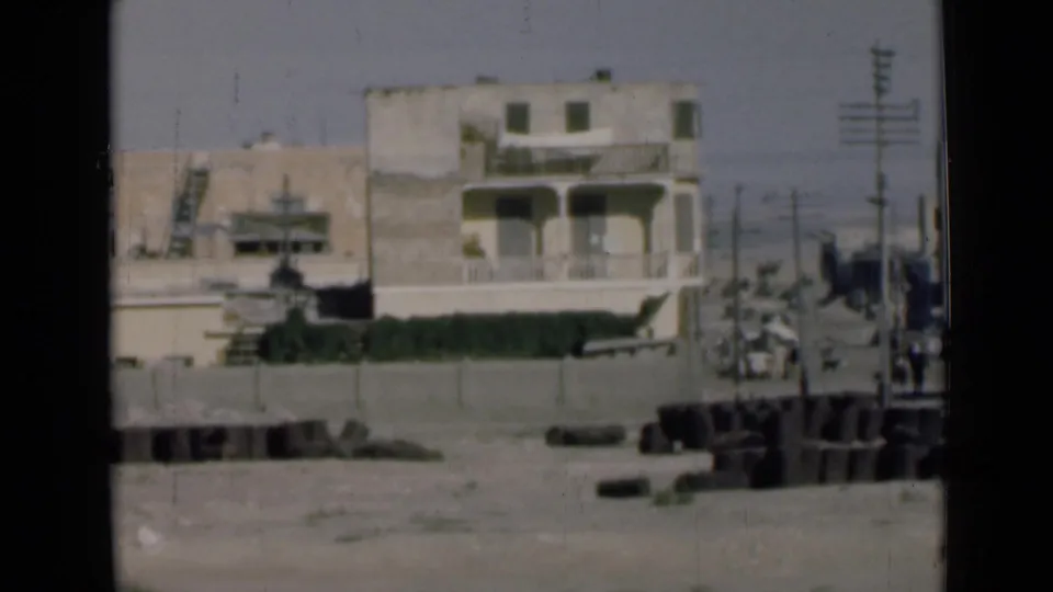 1946 Suez Canal, Egypt street-side view with a balcony building, utility poles, distant pedestrians, and foreground debris.