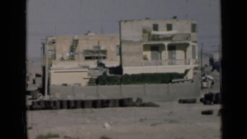 1946 Suez Canal, Egypt view of pale stucco buildings with balconies behind a wall, with debris along the road edge.