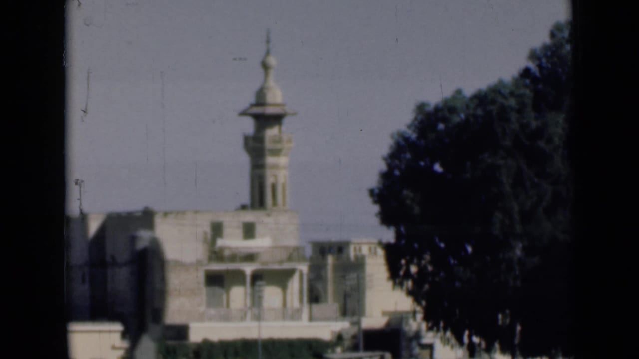 1946 Suez Canal area home-movie frame showing a light-colored building with a minaret, seen from a moving vehicle beside a large tree.