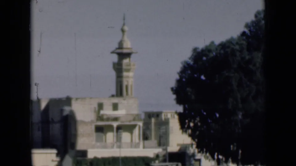 1946 Suez Canal area home-movie frame showing a light-colored building with a minaret, seen from a moving vehicle beside a large tree.