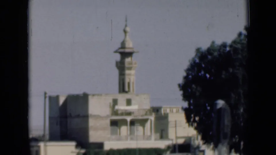 A 1946 Egypt travel frame shows the minaret and upper facade of a pale building, with a large tree and soft motion blur from the vehicle.