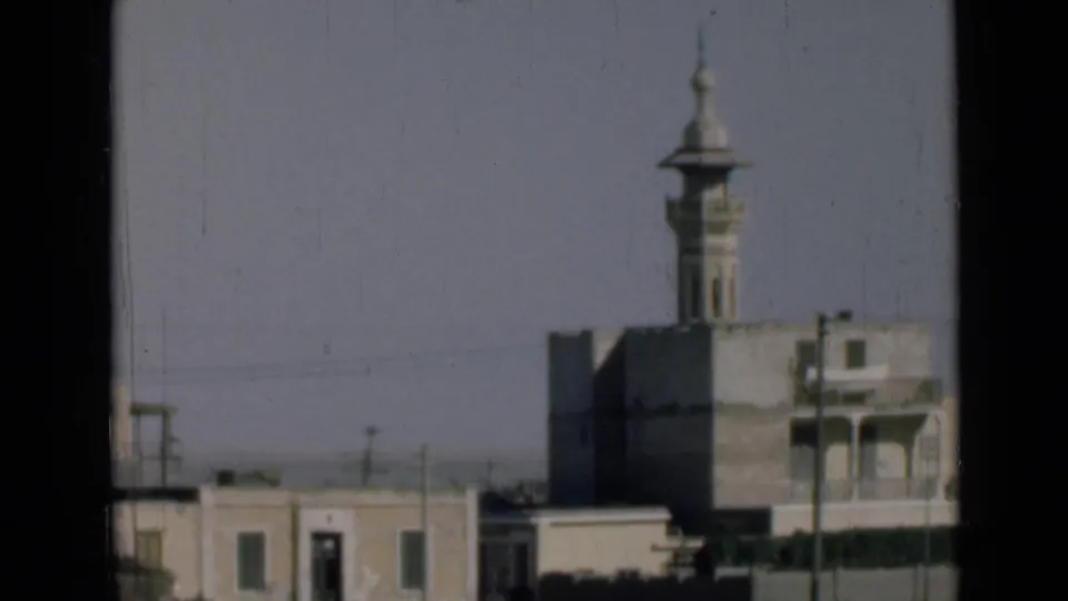 A moving 8mm view in the Suez Canal area shows a minaret above surrounding buildings, partially bordered by dark window framing.