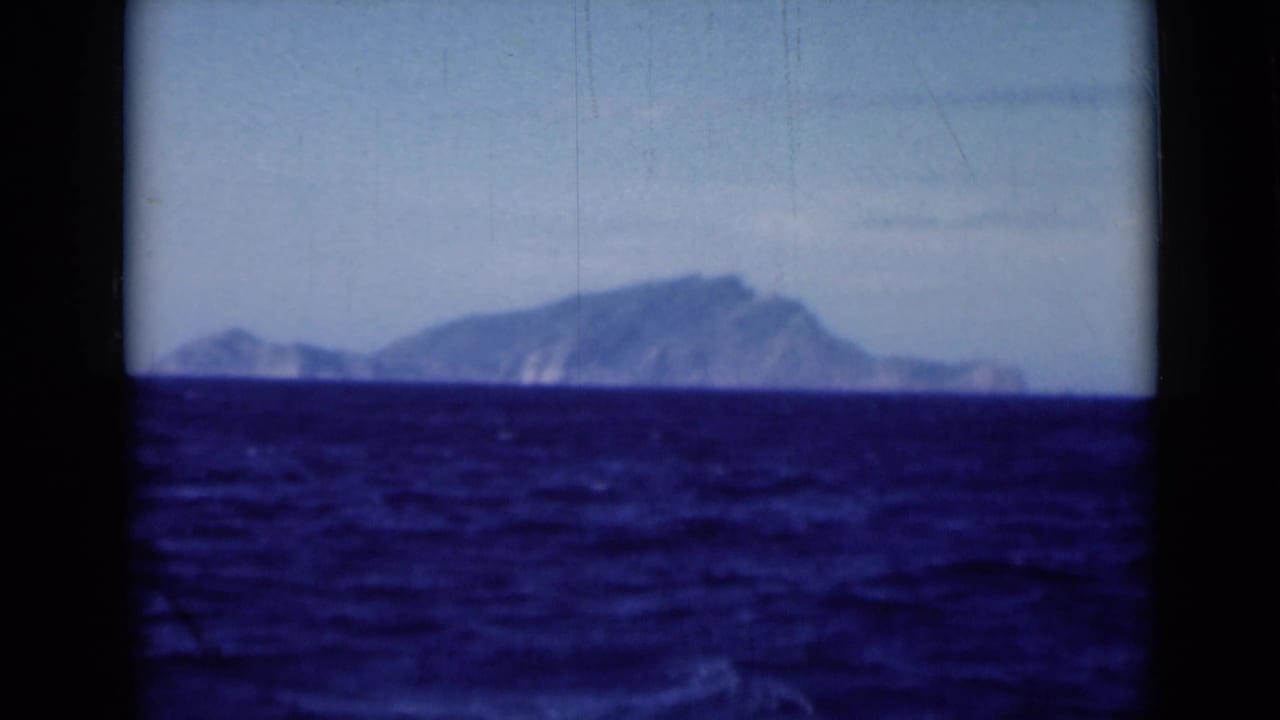 Hazy mountain island or coastline seen over rippled blue water.