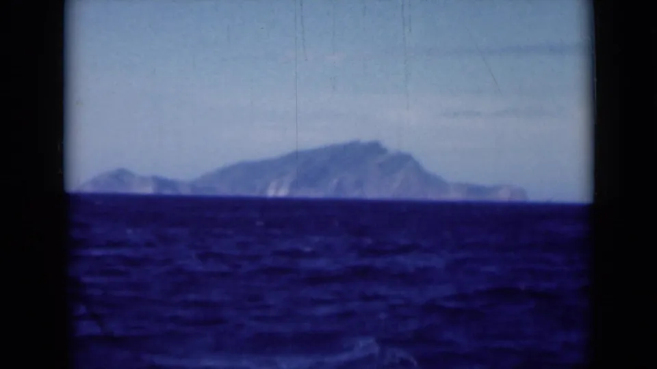 Shipboard 8mm view near the Suez Canal region, with a distant hazy mountain profile beyond rippled blue sea.
