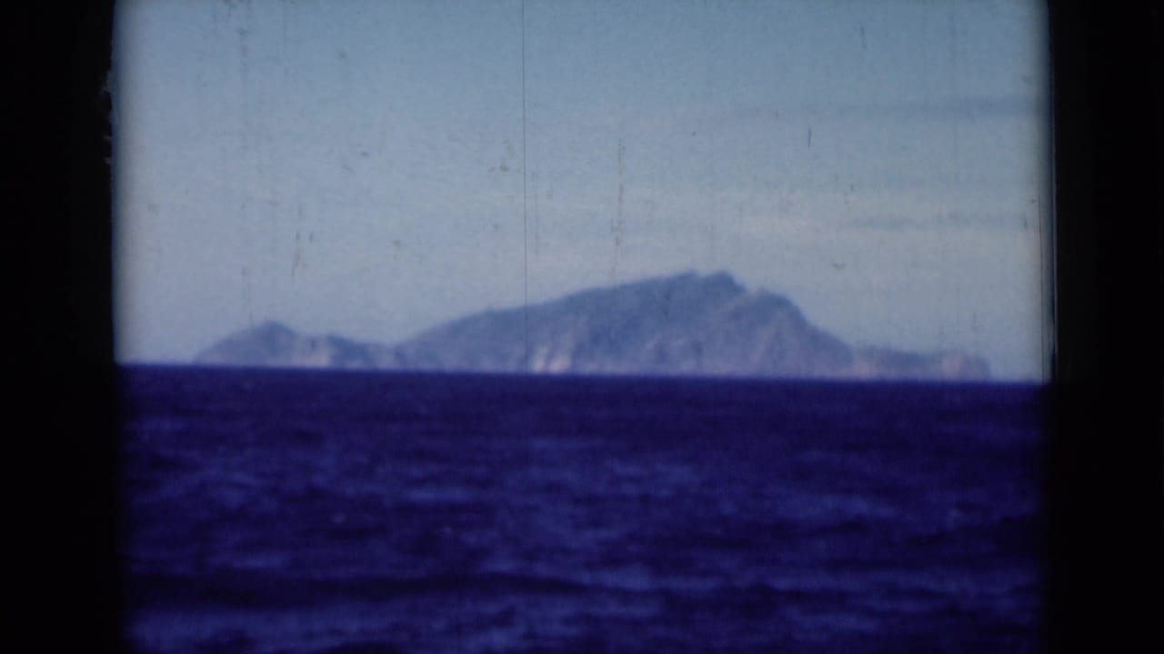 1946 Suez Canal area home-movie frame showing a distant landmass beyond dark blue water, framed by ship-window edges.