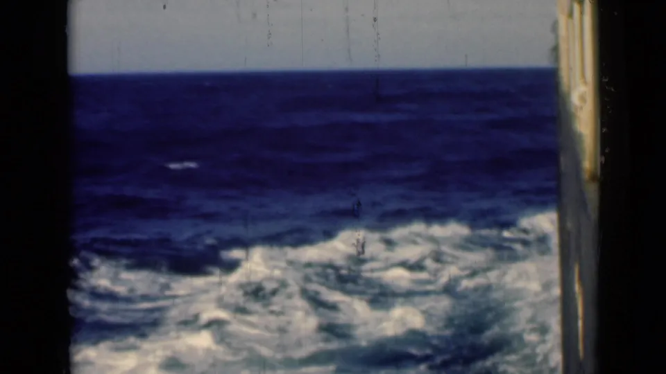 1946 shipboard travel frame showing open water, wake foam, horizon, and a narrow strip of vessel along the right edge.