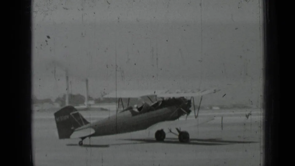 1937 San Francisco-area home-movie frame showing a biplane parked on an open tarmac with soft focus and film wear.