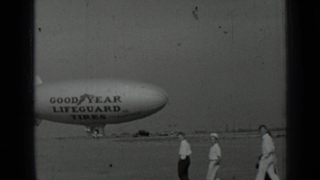 Goodyear Lifeguard Tires blimp with people walking across the airfield.
