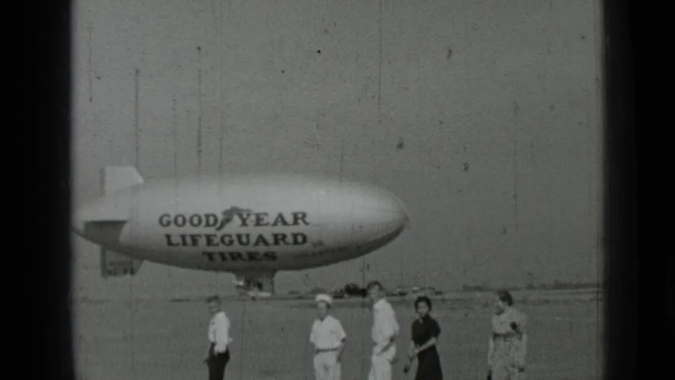 1937 San Francisco-area home-movie frame showing a small group of people in front of a Goodyear Lifeguard Tires blimp.