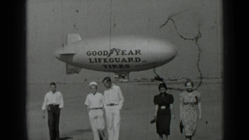1937 San Francisco 8mm frame showing five adults approaching the camera below a Goodyear Lifeguard Tires blimp.