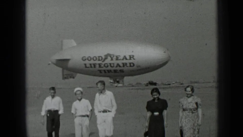 In 1937 San Francisco home-movie footage, five people walk on an airfield in front of a Goodyear Lifeguard Tires blimp.