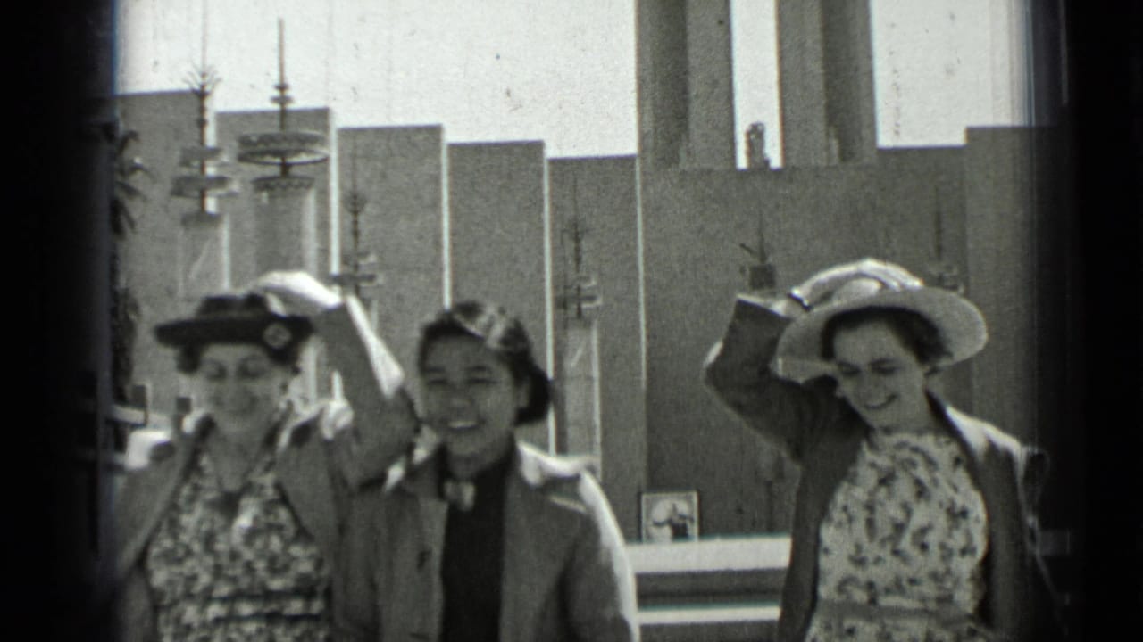 Women in hats pass the camera as one adjusts her hat near church architecture.