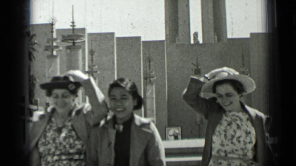 Three women in vintage attire move down the church steps, with one holding her hat against the sun or wind.